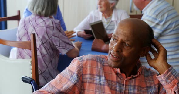 Thoughtful senior man sitting in wheelchair while senior friends interacting in background 4k