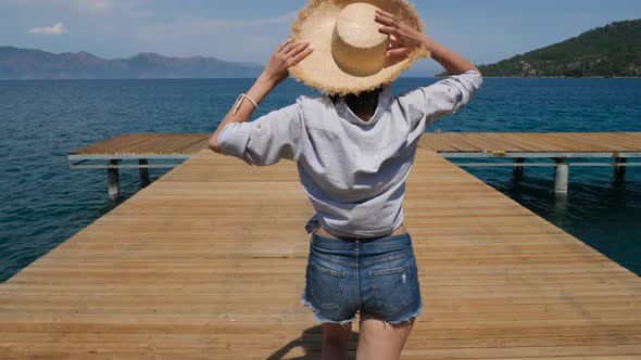 Young Sexy Girl in a Hat and Shorts Walking on the Pier