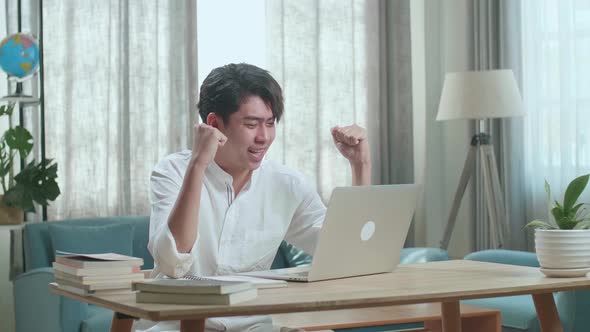 Asian Man Student Celebrating While Using Computer To Study Online At Home