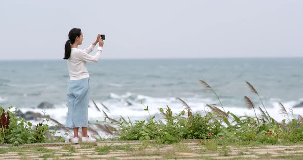 Woman taking photo on cellphone with the sea