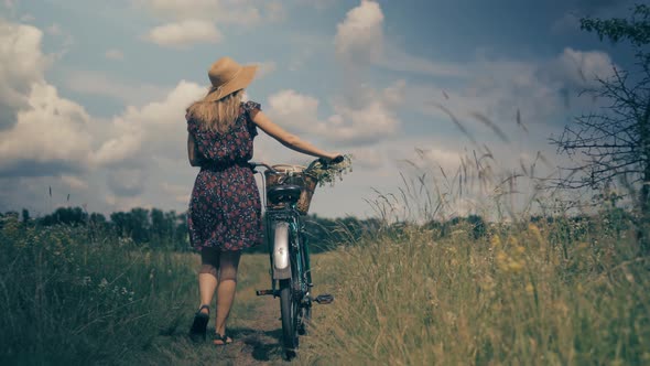 Tourist Girl Relaxing On Countryside Wildflower Field. Woman Cyclist Walking With Bike On Holiday.