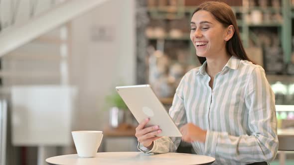 Excited Young Latin Woman Celebrating Success on Tablet in Cafe