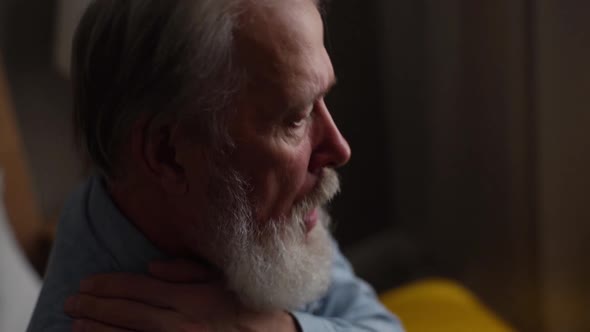 Closeup Face of Sick Grayhaired Mature Adult Male Coughing Violently Into Arm at Home Alone in Dark