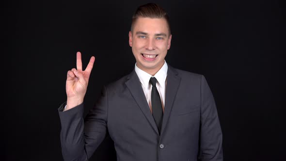 Young Businessman Shows Victory Sign with His Hand. Man in a Black Suit on a Black Background