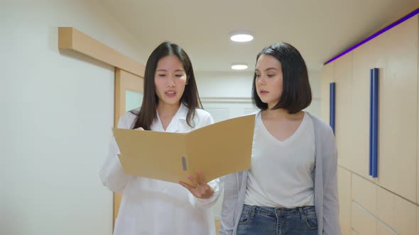 Asian female doctor or dentist talking to woman patient walking on hallway in hospital or clinic.