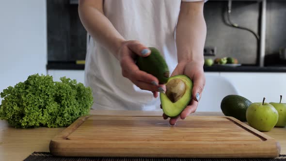 Close Up Women s Hands Hold Two Cut Halves of Fresh Green Avocado of the Kitchen Background