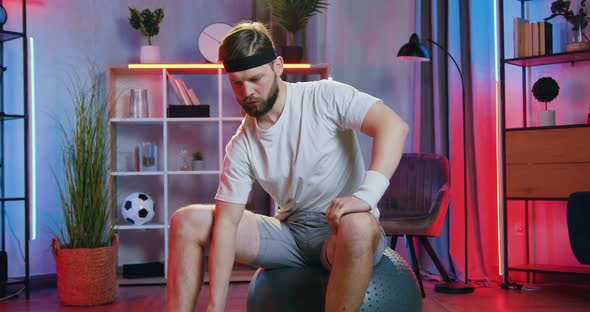 Man in Sportswear Sitting on Fitball and Doing Exercises with Dumbbells to Keep His Body Healthy
