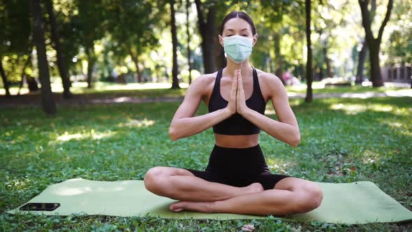 Athletic Young Woman in a Medical Protective Mask Doing Yoga in the Park