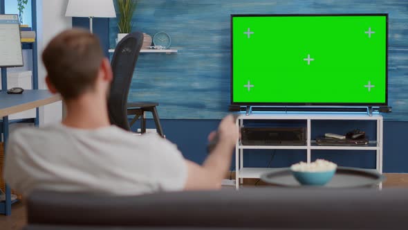 Static Tripod Shot of Man Switching Channels While Looking at Green Screen on Tv