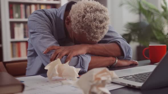 Tired Dark Skinned Man Sleeping at Workplace Placing Head on Documents