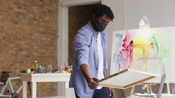 African american male artist wearing face mask using laptop at art studio