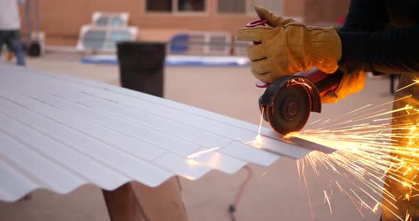 A construction worker using a power tool angle grinder to cut metal and send glowing bright sparks f