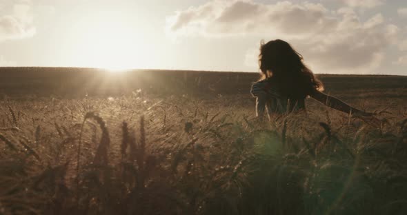 young girl in a golden field during sunset raising her hands in happiness