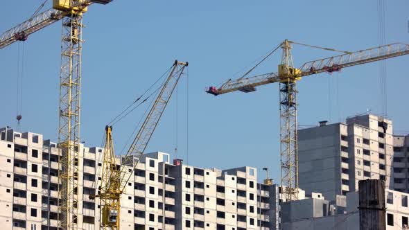 Yellow Construction Cranes and Buildings Over Blue Sky Background