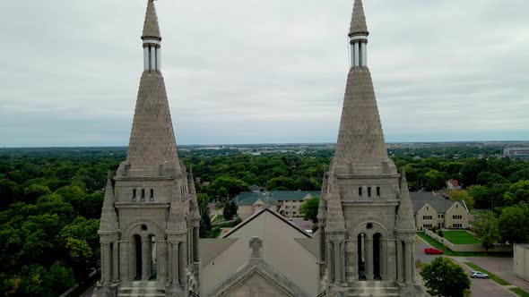 Drone view bringing front of cathedral with twin steeples into view. Many trees along the streets.