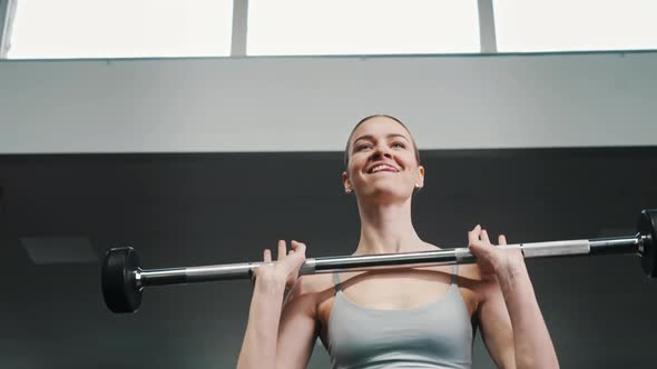 a Portrait of a Fit Girl in a Gray Sports Coat Does Exercises with Dumbbells Under the Supervision