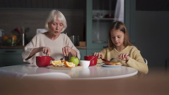 Positive grandmother and granddaughter eating breakfast