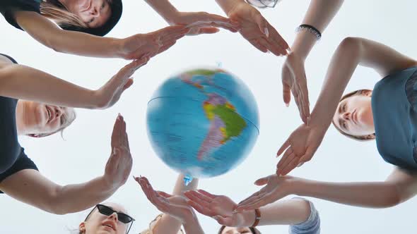 Schoolgirls Hug the Earth Globe with Their Hands Making a Circle Out of Them on the Background of