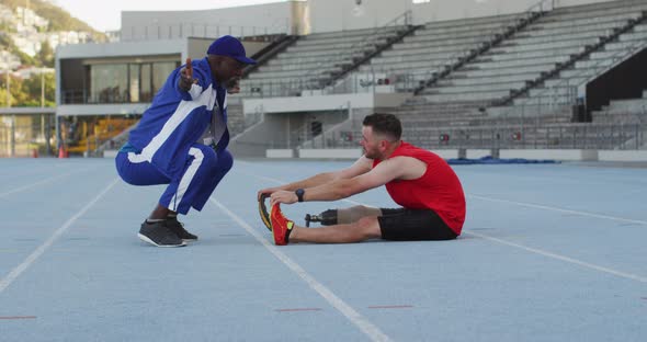 Diverse male coach and disabled athlete with prosthetic leg training and stretching