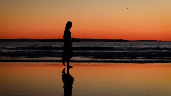 Asian woman enjoys a walk on the beach at sunset. Slow Motion.