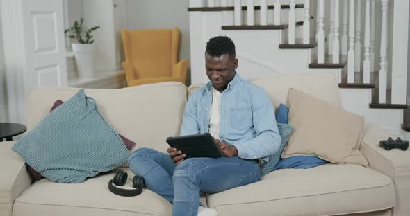 Man in Casual Clothes Resting on Comfortable Sofa in Living-Room and Working on Tablet