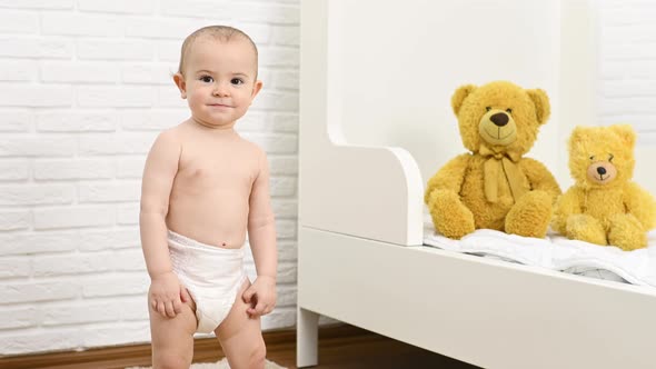 Baby Boy in a Disposable Diaper Smiles and Takes the First Steps