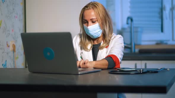 Modern Female Doctor in Medical Mask Using Laptop and Phone During Home Visit