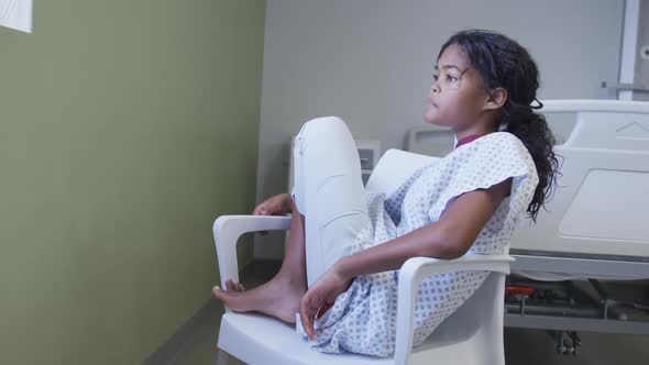 Mixed race girl sitting on chair in hospital patient room looking through the window