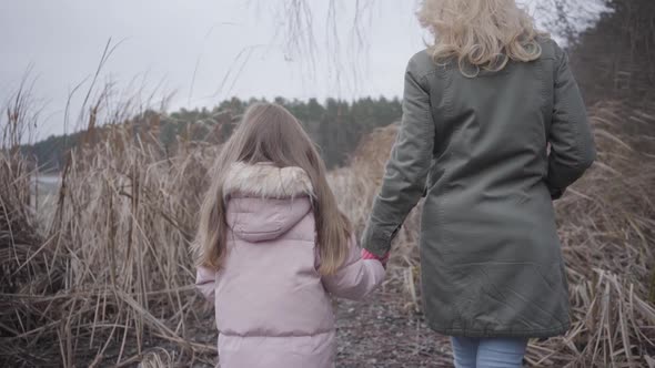 Back View of Caucasian Woman and Girl Walking To the Lake or River Through Bushes. Blond Mother and