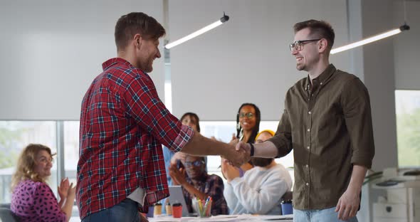 Young Businessmen Handshake on Team Meeting with Group of People Applauding in Modern Startup Office