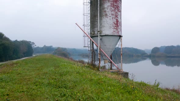 Drone shot of an old metal silo overlooking a reflective lake on an autumn morning