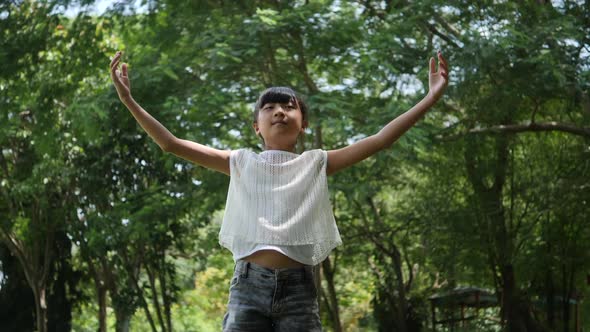 Asian little girl playing outdoor in slow motion, Spinning and smiling and raising hands in the air