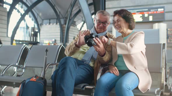 Aged Lovely Couple Waiting for Boarding Inside Airport and Using Digital Camera