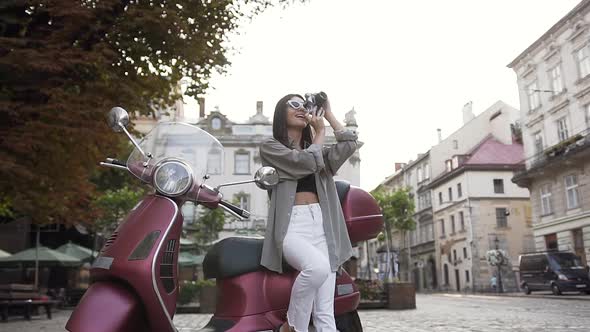 Woman in Stylish Sunglasses Taking Photo on Camera and Sitting on the Modern Scooter