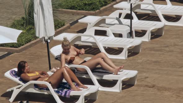 Beautiful Young Women Relaxing on the Deck Chair Near the Pool