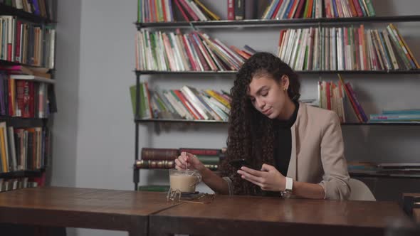 Young Businesswoman Calls Someone On Her Mobile Phone While Having Coffee Break In The Office