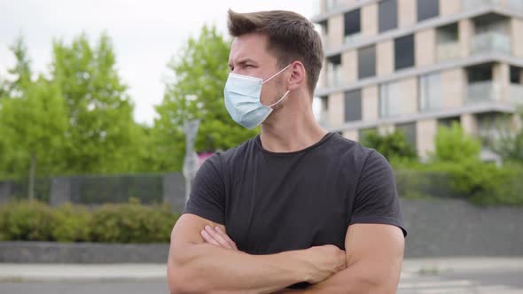 A Young Handsome Man in a Face Mask Looks Around in a Street in an Urban Area