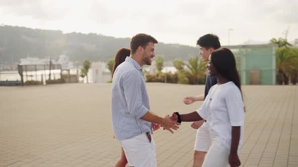 Four Happy Multiracial Millennial Friends Greeting Each Other Outdoors on Summer Day