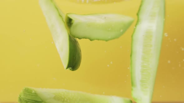 Cucumber Cut In Lengthwise Falls Into The Water In Yellow Background. - close up, studio shot