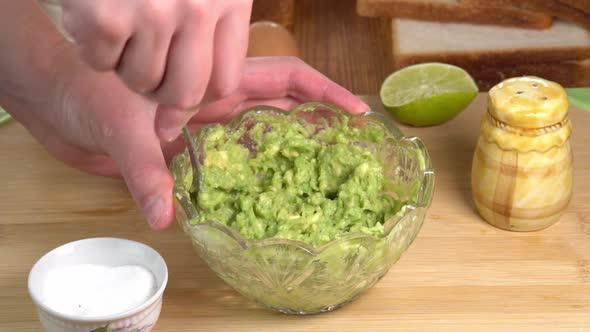 Male chef hands preparing guacamole recipe, hands mashing avocado with fork in a bowl. Cooking