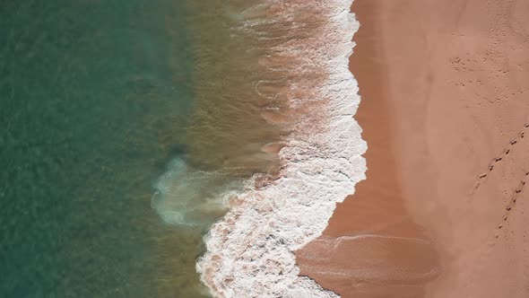 Aerial view of sandy portuguese beach with rolling waves; sunny day, top down view