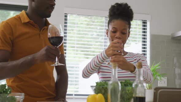 Video of happy african american couple cooking together in kitchen with wine