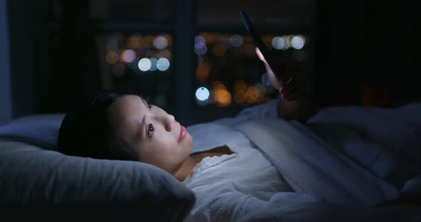 Woman use of mobile phone on bed at night