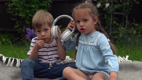 Two Happy Siblings Boy Ans Girl Listening to Music on Headphones Outside in Garden