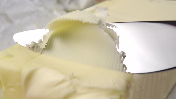 A kitchen knife cuts a piece of butter with a curl