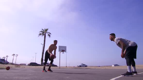 A man takes a layup shot while playing one-on-one basketball hoops on a beach court.