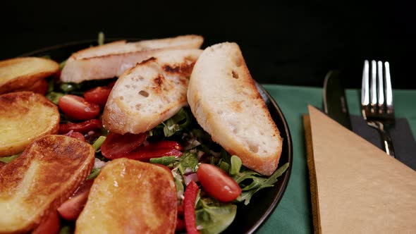 Delicious fresh salad is served with roasted garlic bread on black plate. Restaurant food scene.