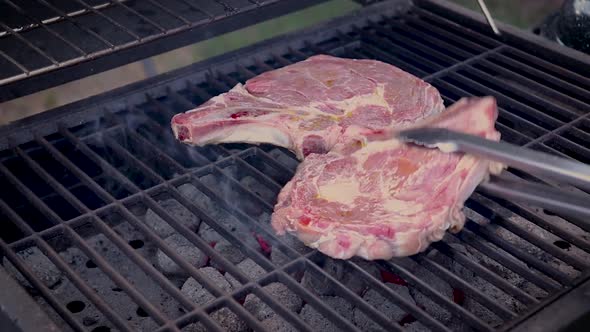 Raw steaks grilling on a charcoal barbecue while seared on one side.