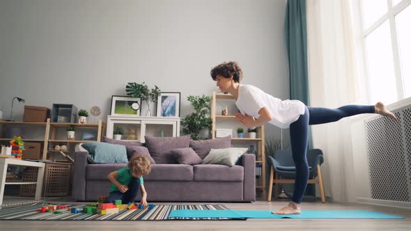 Small Boy Playing with Blocks While Mother Pretty Girl Doing Yoga Balancing