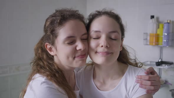 Closeup Charming Beautiful Twin Sisters Hugging Looking at Camera